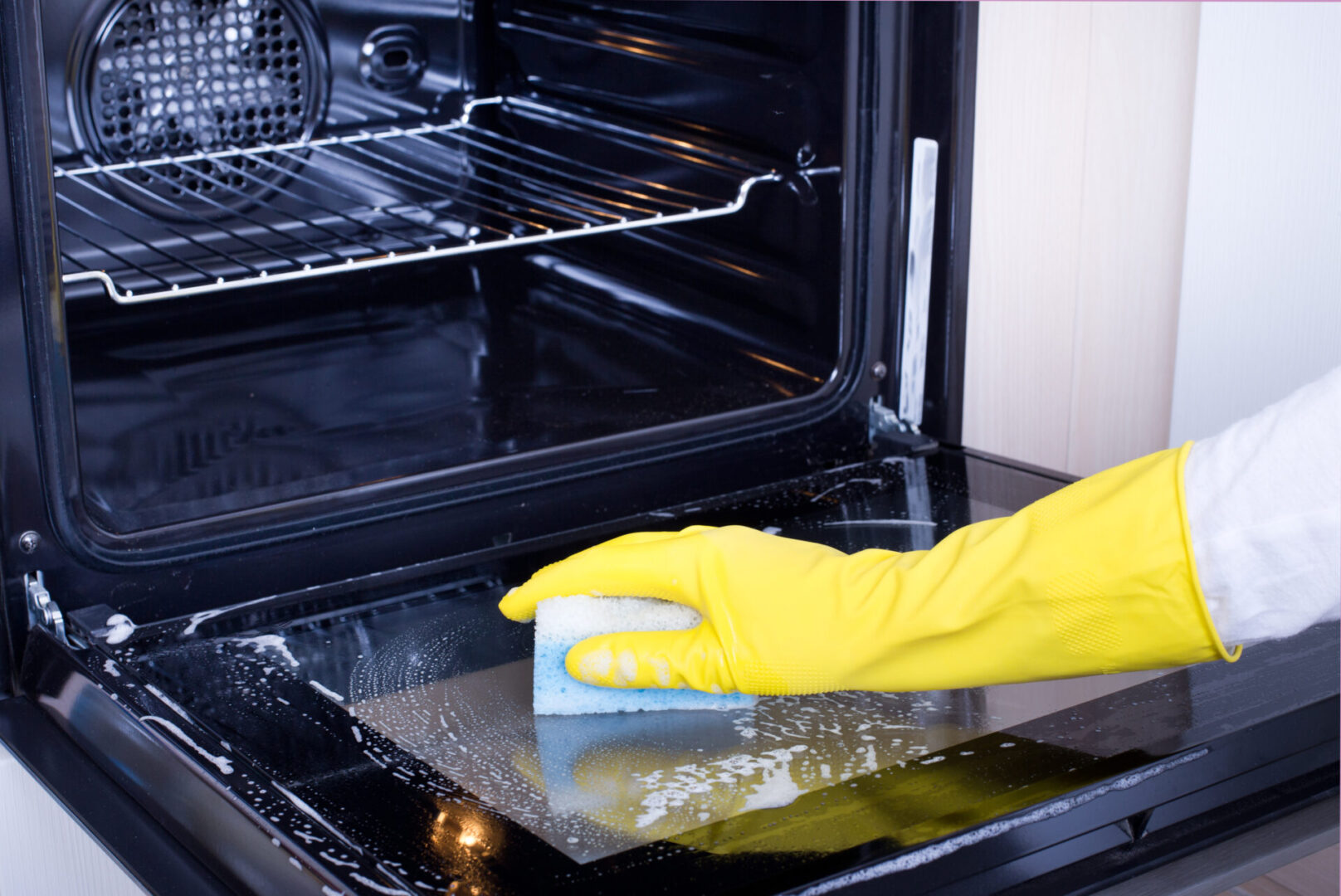 A person cleaning an oven with a sponge.