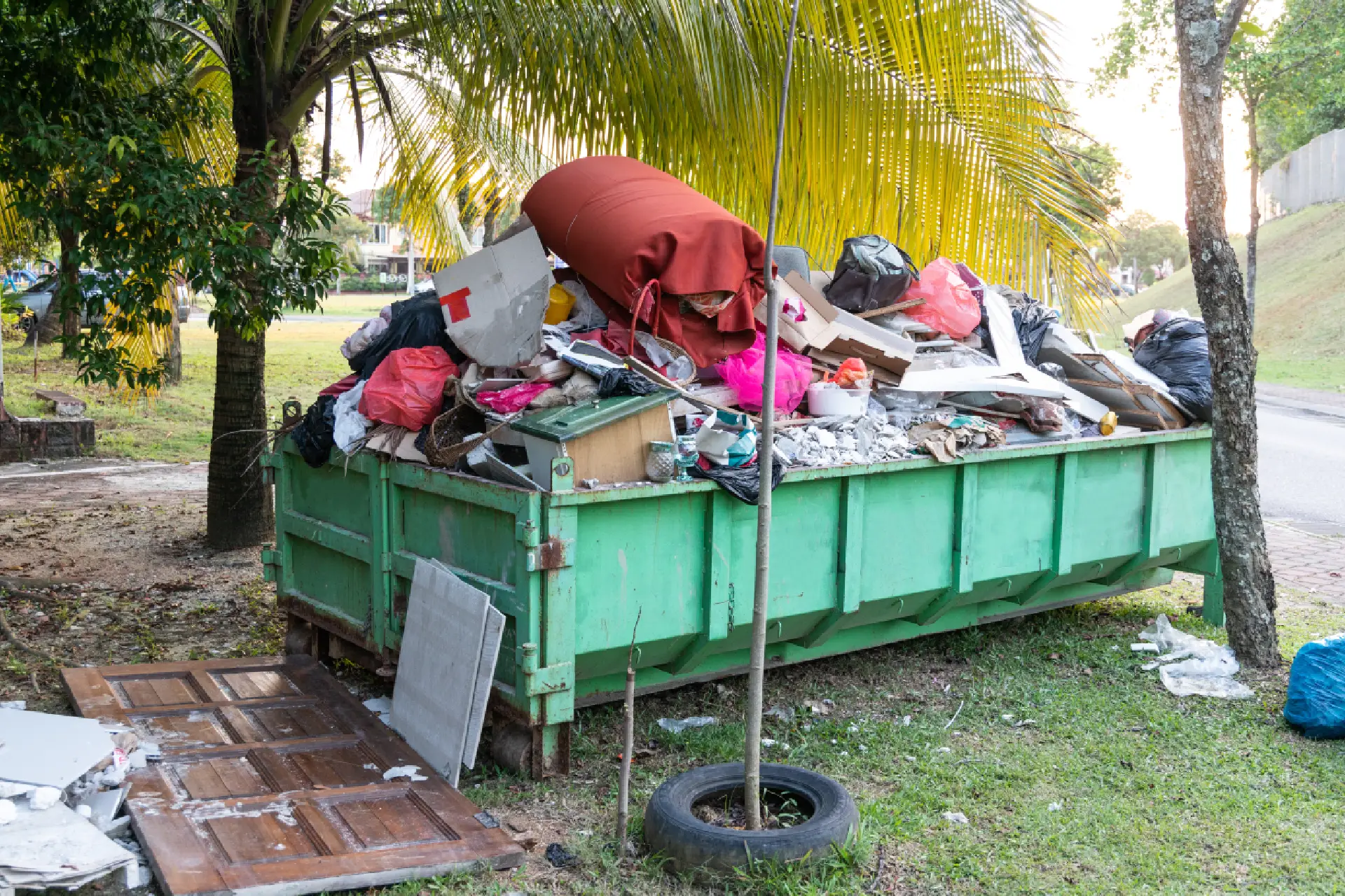 A dumpster full of trash next to a tree.